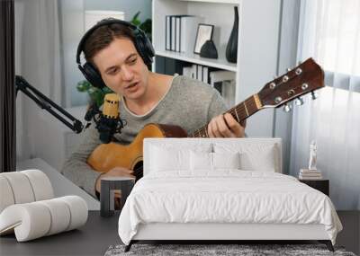 Host channel in smart singer with smiling face, playing guitar along singing, broadcasting on social media channel, wearing headphones to record video streamer at modern studio recording. Pecuniary. Wall mural