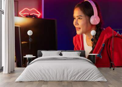 Host channel of smiling beautiful Asian girl streamer playing online game wearing headphone talking with viewers media online recording phone. Esport skilled team players in neon blue room. Stratagem. Wall mural