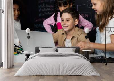 In classroom student in STEM class learning about coding robotics car. Brown shirt Schoolboy and white bib schoolgirl watching laptop and discussing. Other schoolgirls playing around funny. Erudition. Wall mural