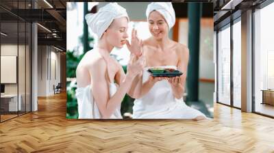 Portrait of two attractive woman in towel giggling during hold the herbal bowl surrounded by natural spa environment. Pretty girls with beautiful skin using herbal scrub at spa salon.Tranquility. Wall mural