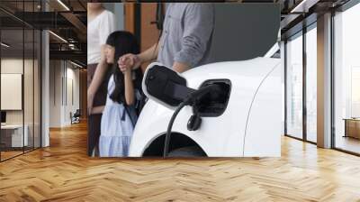 Progressive parent have returned from picking up daughter at school with concept of electric vehicle and renewable energy, charging station for EV car at home. Alternative eco transportation. Wall mural