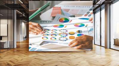 Skilled architect searching data from tablet while selecting an appropriate color from color wheel at table with color palette and document scatter around. Creative design concept. Variegated. Wall mural