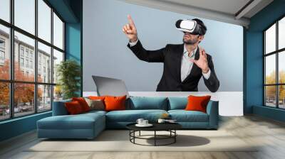 Skilled business man looking at data analysis while sitting at table with laptop and wearing VR glasses. Project manager working by using virtual reality system or connecting at metaverse. Deviation. Wall mural