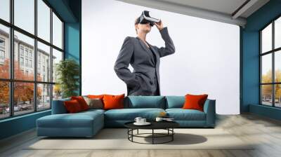 Skilled businesswoman looking at visual reality world by using VR glass while standing at background. Smart manager holding VR goggle to connect metaverse by using technology innovation. Contraption. Wall mural