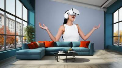 Smart female standing with gray background wearing VR headset connecting metaverse, futuristic cyberspace community technology. Elegant woman excited seeing generated virtual scenery. Hallucination. Wall mural