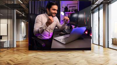 Smart trader businessman concentrating on dynamic stock exchange investment on pc and laptop showing on screen with high profit in searching market at neon light office in dark room night. Surmise. Wall mural