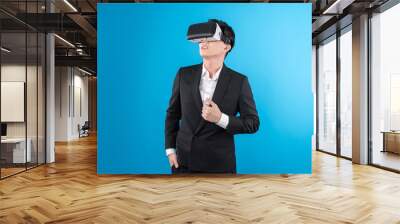 Smiling Asian businessman looking thorough VR connecting to business world report in futuristic metaverse, analyzing innovation technology ads in virtual reality isolated blue copyspace. Contrivance. Wall mural