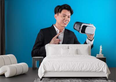 Smiling Asian businessman looking through VR connecting financial business report futuristic metaverse data analytics power bi technology virtual reality meta isolated blue copyspace. Contrivance. Wall mural