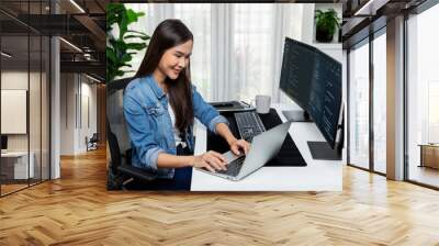 Smiling young Asian in IT developer creating with typing online information on laptop with coding program data of application, wearing jeans shirt. surrounded by safety analysis two screen. Stratagem. Wall mural