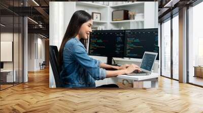 Smiling young Asian in IT developer creating with typing online information on laptop with coding program data of application, wearing jeans shirt. surrounded by safety analysis two screen. Stratagem. Wall mural