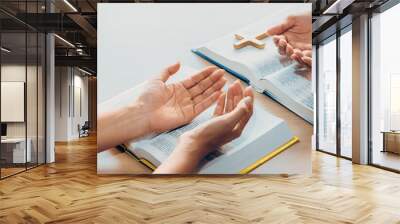 Two believer praying together on holy bible book faithfully with wooden cross placed at wooden church. Concept of hope, religion, faith, christianity and god blessing. Facing hand. Burgeoning. Wall mural