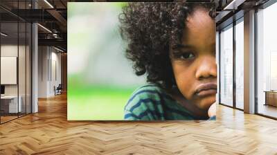 Unhappy bored little african american kid sitting in the park. The boy showing negative emotion. Child trouble concept. Wall mural