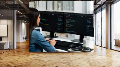 Young Asian in IT developer creating with typing online information on pc with coding program data of website application, wearing jeans shirt. surrounded by safety analysis two screens. Stratagem. Wall mural