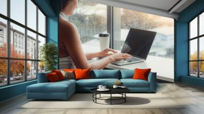 Young business woman using laptop computer while sitting at cafe table next to office windows. Wall mural