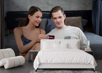 Young couple sit in the home bedroom using online payment app and digital wallet on smartphone to pay with credit card. E commerce shopping and modern purchasing via mobile internet. Unveiling Wall mural