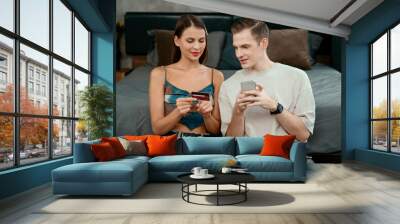 Young couple sit in the home bedroom using online payment app and digital wallet on smartphone to pay with credit card. E commerce shopping and modern purchasing via mobile internet. Unveiling Wall mural