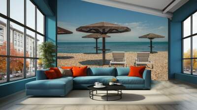 two white sun loungers under a wooden beach umbrella on a rocky beach in summer on a clear day without people Wall mural