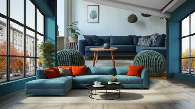 A simple yet chic Scandinavian living room with a dark blue corner sofa and two knitted poufs in forest green, perfectly matching with the natural elements and wooden furniture in the room. Wall mural