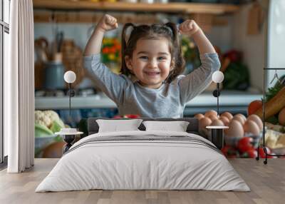 A young girl is smiling and holding her arms up in the air while standing in front of a table full of vegetables Wall mural