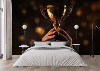 Hands of a man raising golden trophy after winning competition with glowing bokeh on black background, succees concept. Wall mural