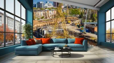 Yellow building crane on the construction site of a large residential modern building at the background of construction site, city buildings and cloudy dramatic sky. Wall mural