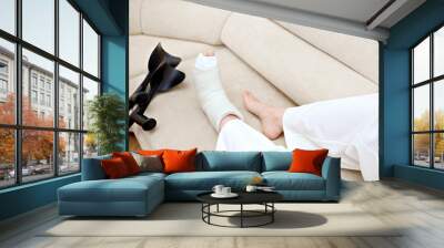 Broken leg in a plaster cast, near a crutches. Youthful woman with a foot bone fracture is taking it easy on the couch. Toe, talus, navicular, cuboid bone fracture. Injury, trauma, recovery concept Wall mural