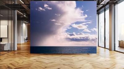 Menacing storm clouds illuminated by sunlight taking over the blue sky and pouring rain on the Pacific Ocean coastline, California Wall mural