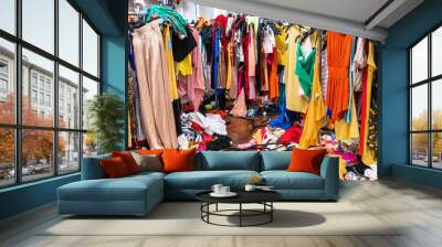 Messy clearance section in a clothing store, with colorful garments on racks and on the floor Wall mural