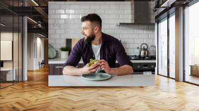 Handsome man eating healthy Mexican food tacos sitting at table at home in modern kitchen and smiling, looking away, copy space Wall mural