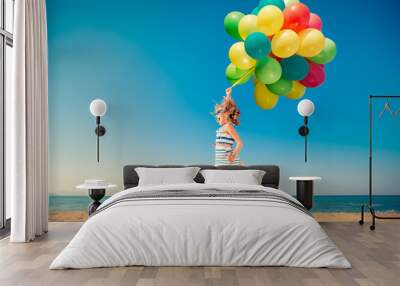 Happy child jumping with colorful balloons on sandy beach Wall mural