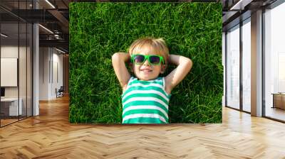 Happy child lying on spring green grass Wall mural