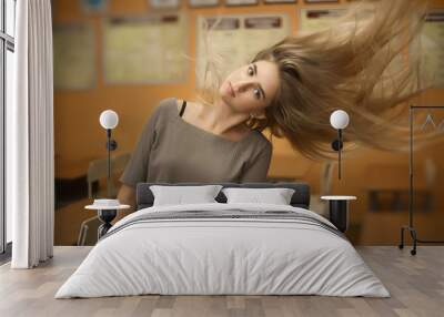 Young student schoolgirl lady shaking her long hair standing in empty classroom looking camera. Wall mural