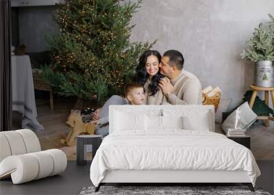 a stylish young beautiful family with a young son is playing on the floor near the christmas tree in Wall mural