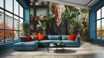 A woman is sitting in a room with plants and a potted plant in front of her. She is meditating and she is in a peaceful and calm state Wall mural