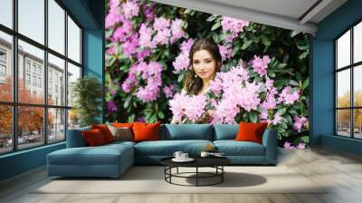 Beautiful young brunette with a smile and big brown eyes in blooming gardens of pink rhododendrons Wall mural