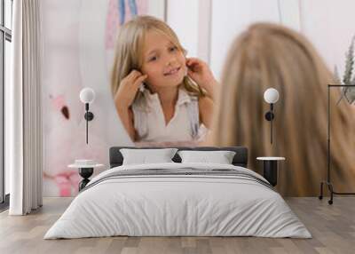 Happy child girl of seven years old puts on earrings in front of the mirror Wall mural