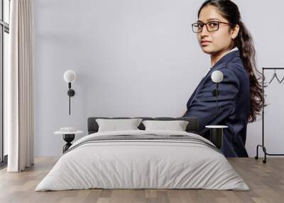 Side view of a college girl in blue suit hands folded and specs looking at the camera. Copyspace Wall mural