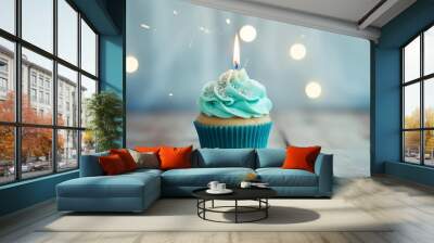 A cupcake with blue frosting and a single candle on a wooden table against a backdrop of out of focus lights. Wall mural