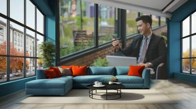 Happy  businessman using cellphone while sitting on sofa at his modern home.Concept of young people working on mobile devices.Blurred background Wall mural