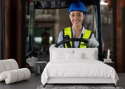 African American female worker driving forklift truck in heavy metal industrial factory. Smiling woman engineer wearing vest and helmet safety moving heavy metal material at warehouse factory. Wall mural