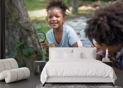 African American little girls with friends exploring and looking bugs on the tree with the magnifying glass between learning beyond the classroom. Education outdoor concept. Wall mural