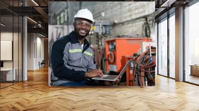 African American male engineer using computer laptop control robot arm welding machine in an industrial factory. Wall mural