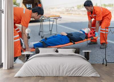 Asian male EMS paramedics or emergency medical technicians in orange uniforms performing first aid to patient on stretcher injured from road accident Wall mural