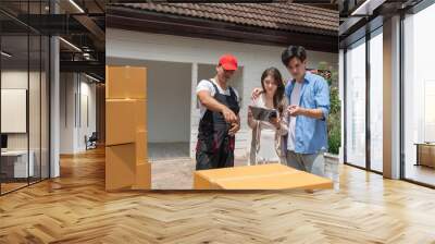 Couple checking cardboard boxes from moving to a new house while man mover worker in black uniform lifting and point to boxes. Professional delivery and moving service. Wall mural