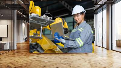 Engineer woman using laptop checking robot arms machine at assembly robotic factory. Female technician in uniform with helmet safety working in automated manufacturing industry Wall mural