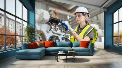 Female automation engineer wear vest with helmet safety using tablet checking and inspection control robot arm welding machine in an industrial factory. Artificial intelligence concept. Wall mural