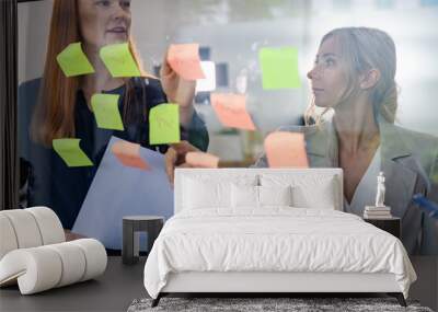 Group of businesspeople brainstorming and writing strategy ideas in post it notes or sticky note on glass wall in office Wall mural