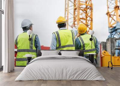 Group of male engineer wearing safety vests and helmet pointing to tower crane for surveying and maintenance at construction site. Wall mural