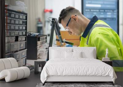 Male electrical engineer using digital multimeter checking voltage on microchip on board of automation robotic arm machine at factory Wall mural