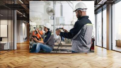 Male engineers control robot arm machine welding steel with remote control in factory workshop. Wall mural